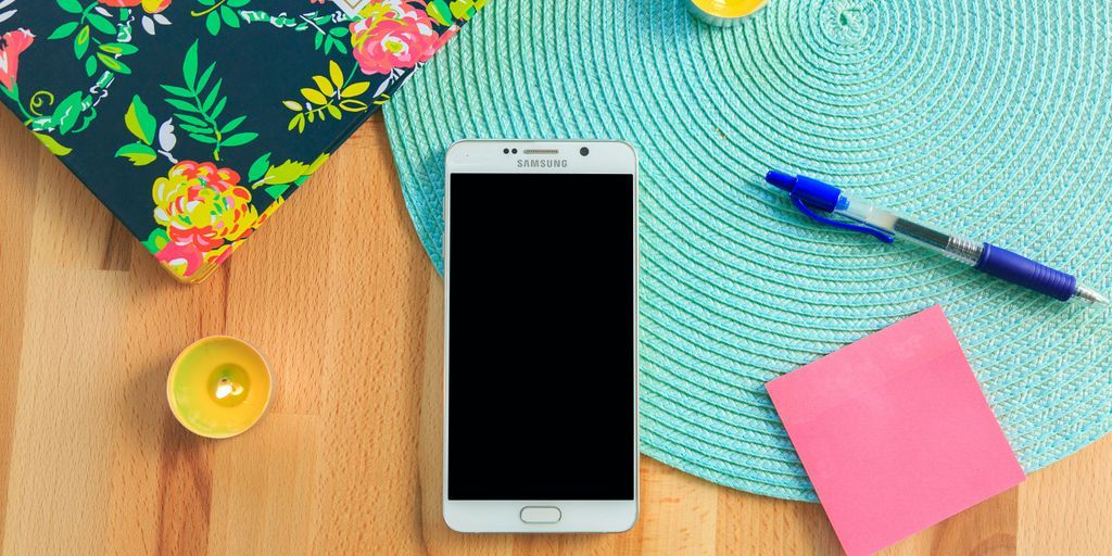 white Samsung Galaxy smartphone on top of blue place mat near blue click pen
